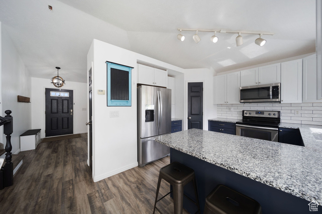 Kitchen with stainless steel appliances, a peninsula, white cabinetry, backsplash, and dark wood-style floors
