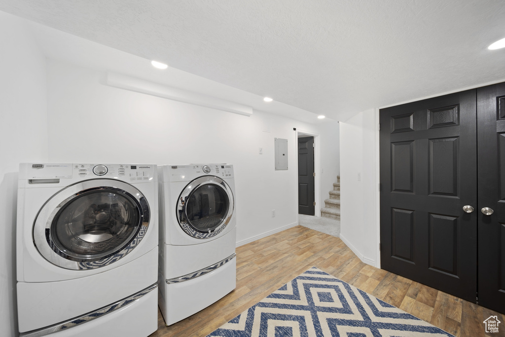 Clothes washing area with electric panel, washing machine and clothes dryer, light wood-style floors, baseboards, and recessed lighting