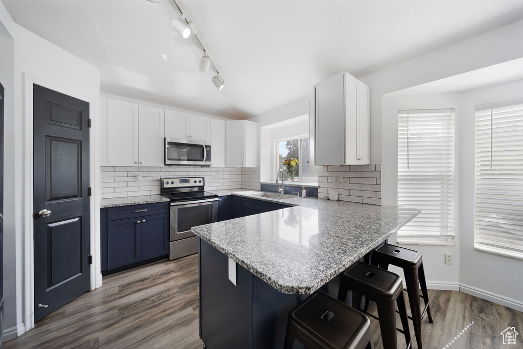 Kitchen with appliances with stainless steel finishes, a kitchen breakfast bar, a peninsula, white cabinetry, and rail lighting