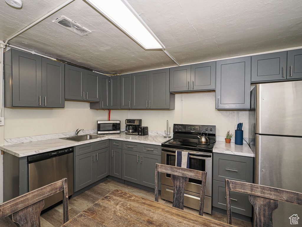 Kitchen with appliances with stainless steel finishes, a sink, dark wood finished floors, and gray cabinetry