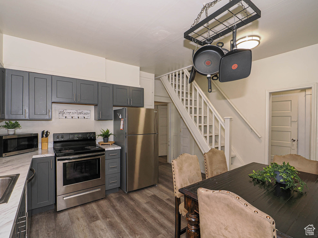 Kitchen featuring stainless steel appliances, dark wood-type flooring, gray cabinets, and light stone countertops