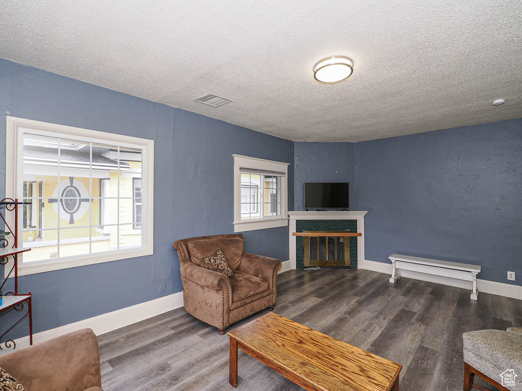 Living room with a textured ceiling, wood finished floors, a glass covered fireplace, and baseboards