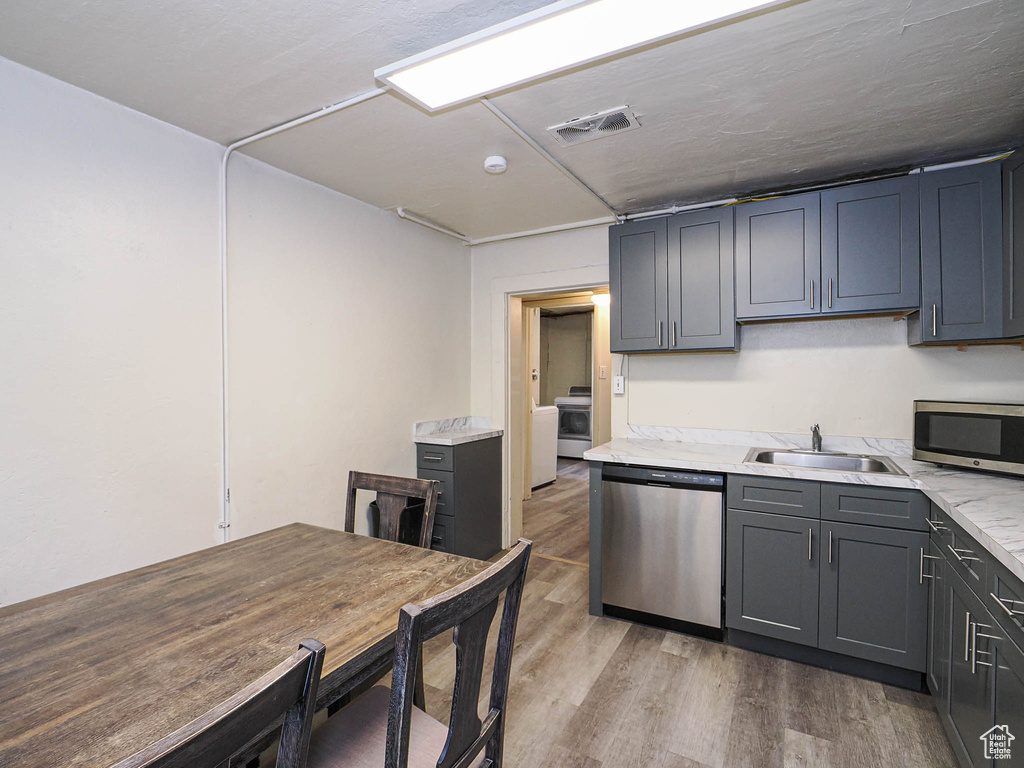 Kitchen featuring appliances with stainless steel finishes, a sink, light wood finished floors, and gray cabinetry
