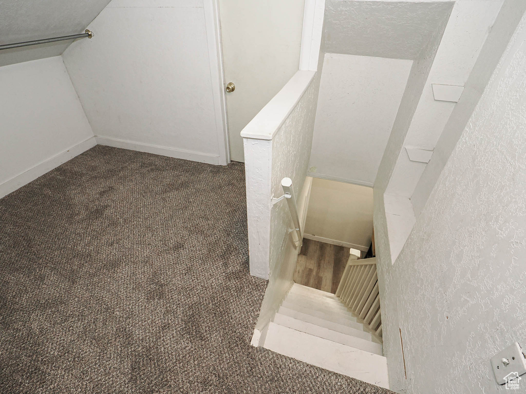 Stairs featuring a textured wall, carpet, and vaulted ceiling