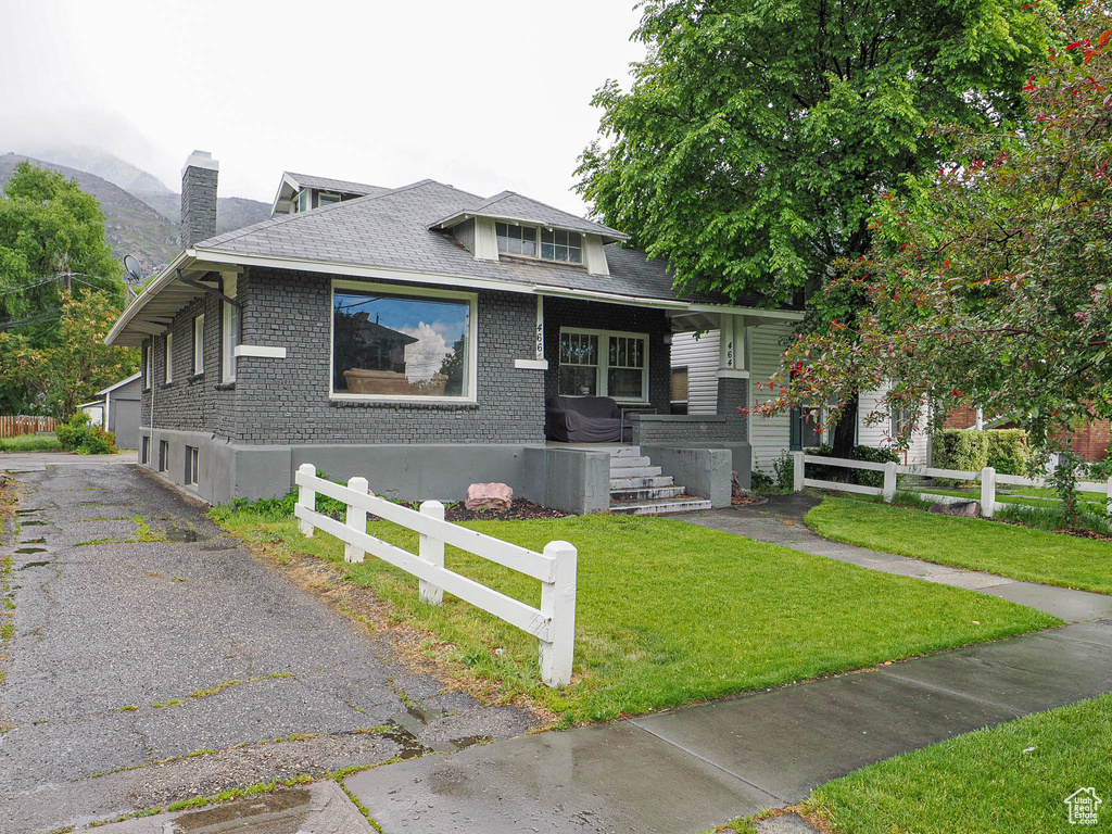 Bungalow with covered porch, a chimney, roof with shingles, and brick siding