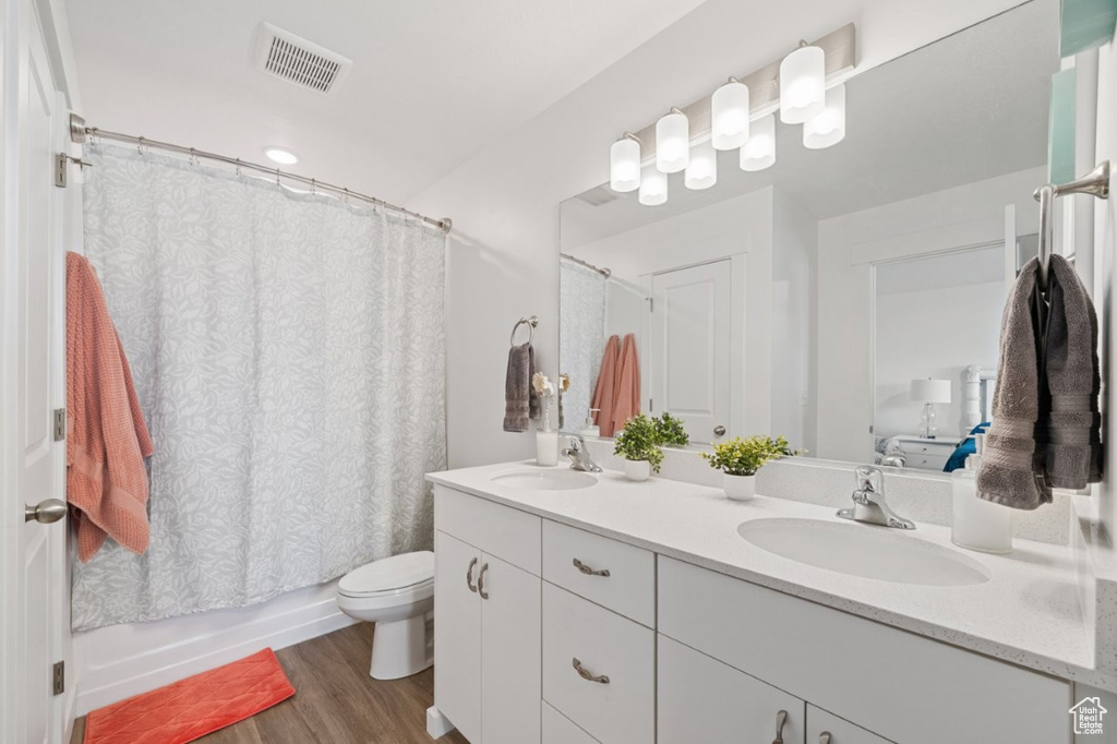 Full bathroom with wood finished floors, double vanity, toilet, and shower / bath combination with curtain