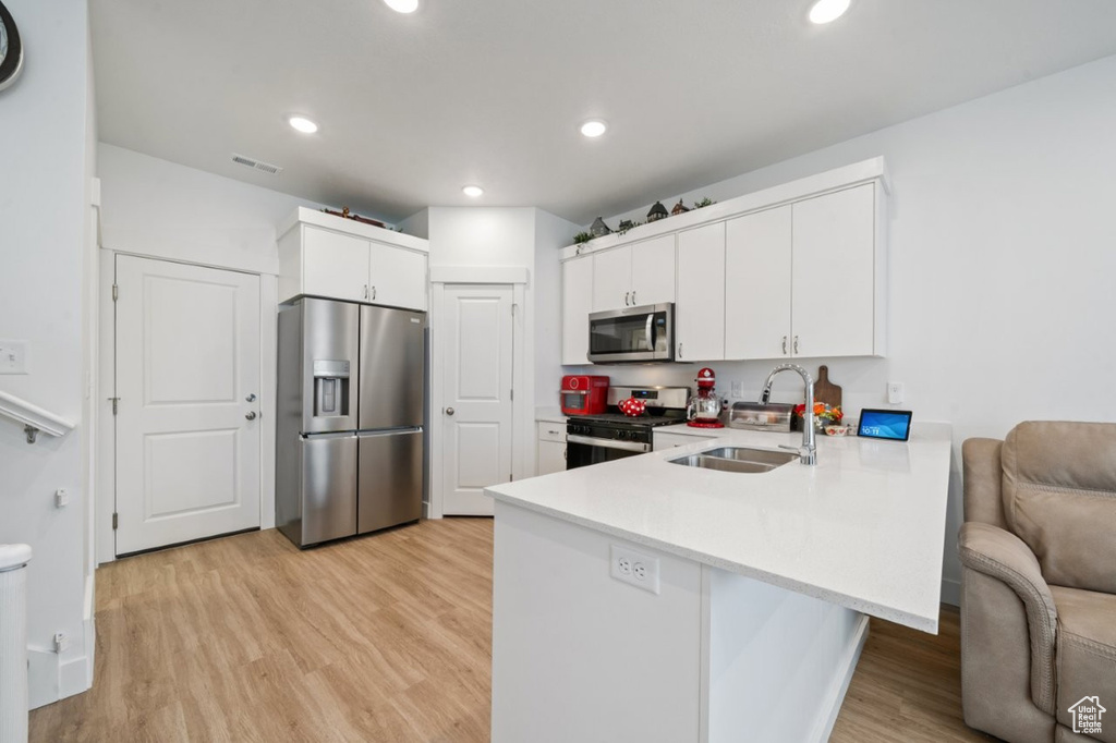 Kitchen with appliances with stainless steel finishes, a sink, a peninsula, light wood-style flooring, and light countertops
