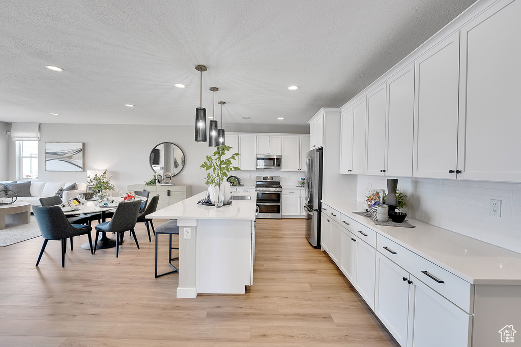 Kitchen with stainless steel appliances, a breakfast bar area, open floor plan, white cabinetry, and recessed lighting