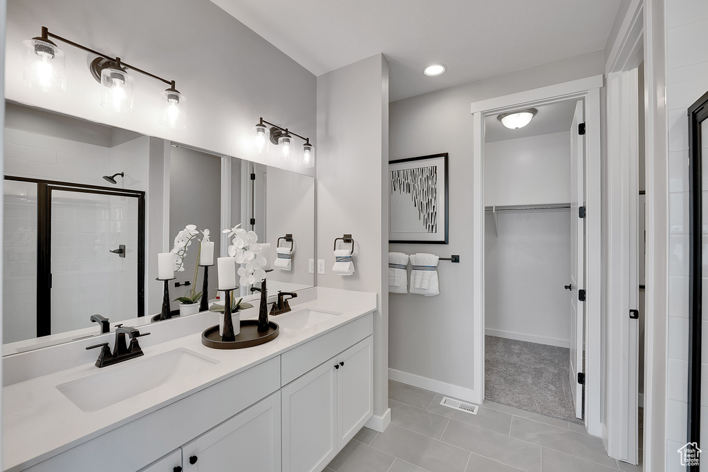 Bathroom with a stall shower, a spacious closet, tile patterned floors, baseboards, and double vanity