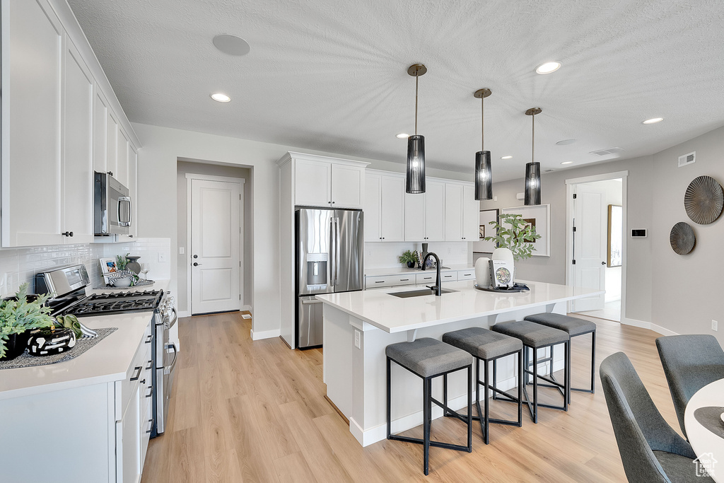 Kitchen featuring appliances with stainless steel finishes, a sink, light wood-style floors, a kitchen bar, and recessed lighting