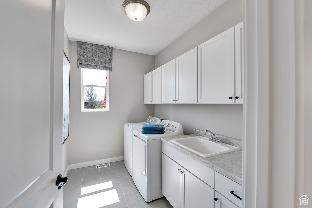 Clothes washing area featuring cabinet space, washer and dryer, baseboards, and light tile patterned floors