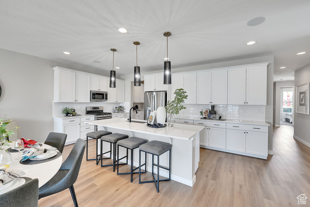 Kitchen featuring appliances with stainless steel finishes, light wood finished floors, a kitchen breakfast bar, light countertops, and recessed lighting