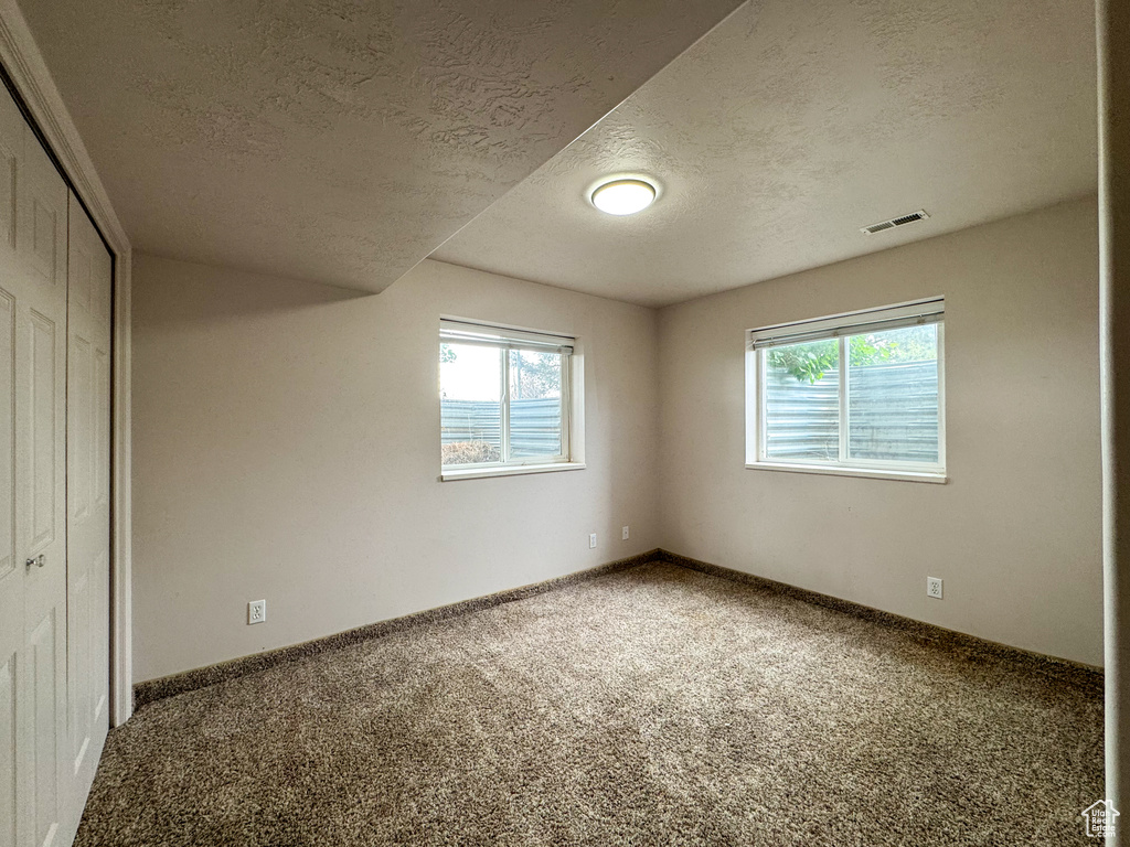 Unfurnished bedroom featuring multiple windows, carpet, a textured ceiling, a closet, and baseboards