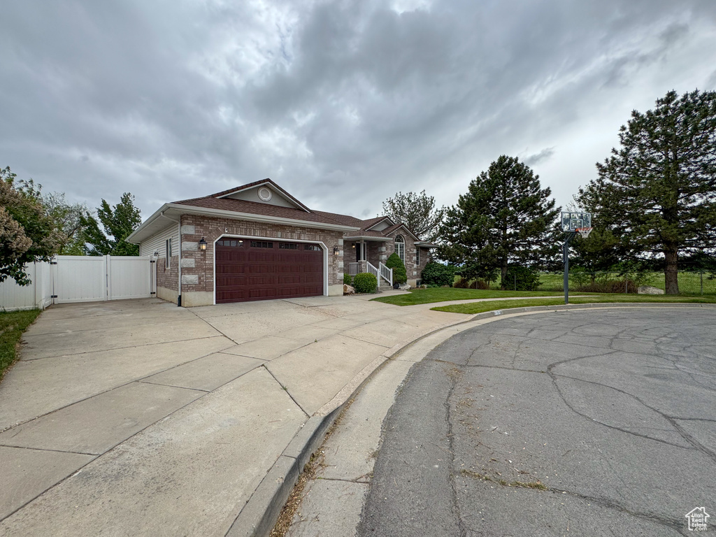 Ranch-style home with a gate, a garage, driveway, brick siding, and fence