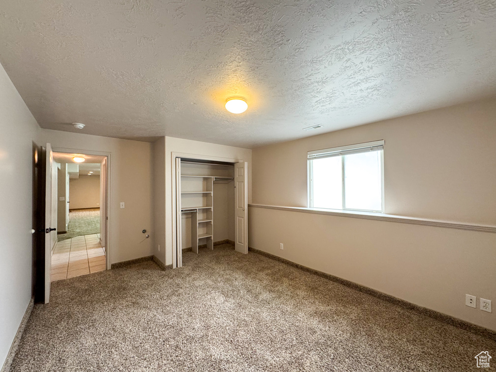 Unfurnished bedroom with a closet, light carpet, a textured ceiling, and baseboards