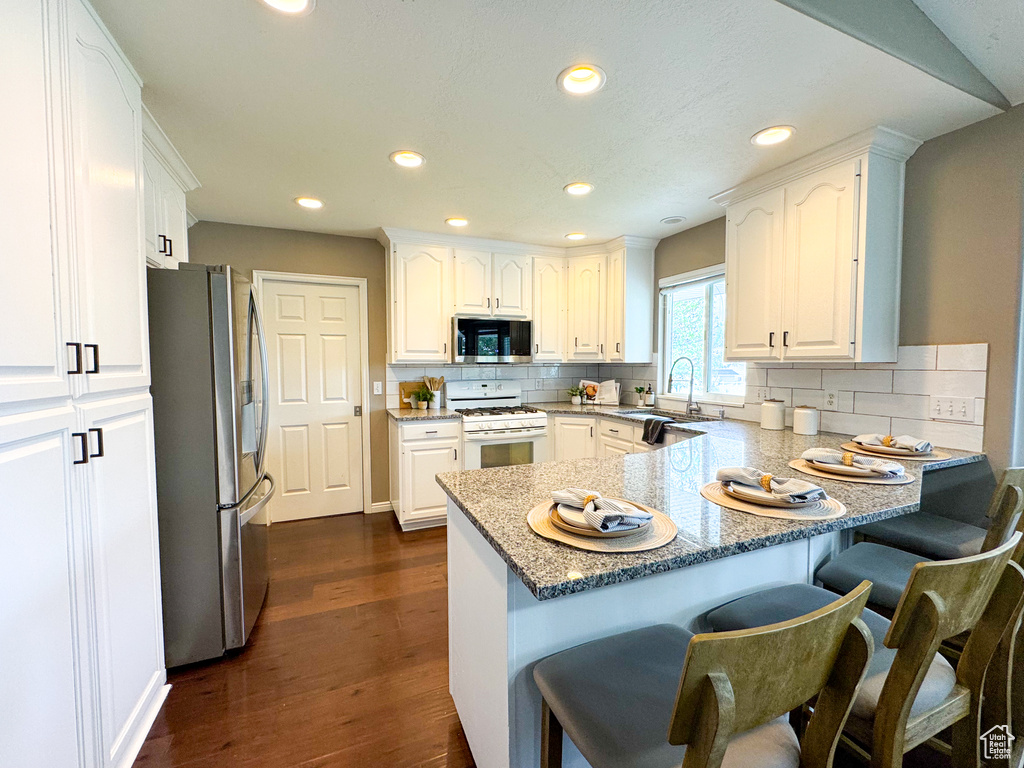 Kitchen featuring stainless steel appliances, a peninsula, a sink, white cabinets, and a kitchen breakfast bar