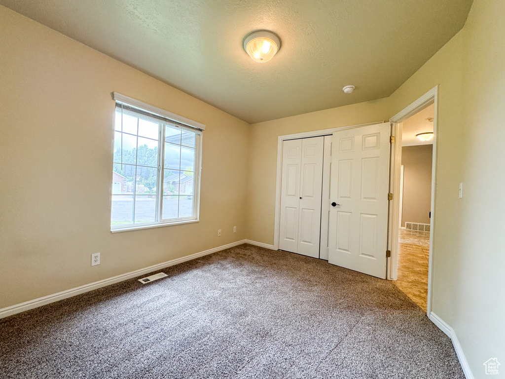 Unfurnished bedroom featuring carpet flooring, baseboards, a closet, and a textured ceiling