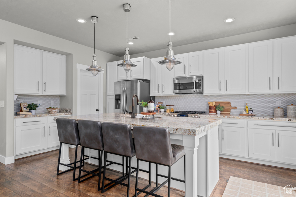Kitchen featuring appliances with stainless steel finishes, a kitchen island with sink, decorative backsplash, dark wood finished floors, and a breakfast bar
