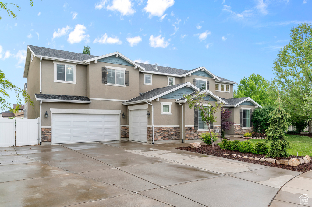 View of front of property featuring stone siding, stucco siding, an attached garage, fence, and driveway