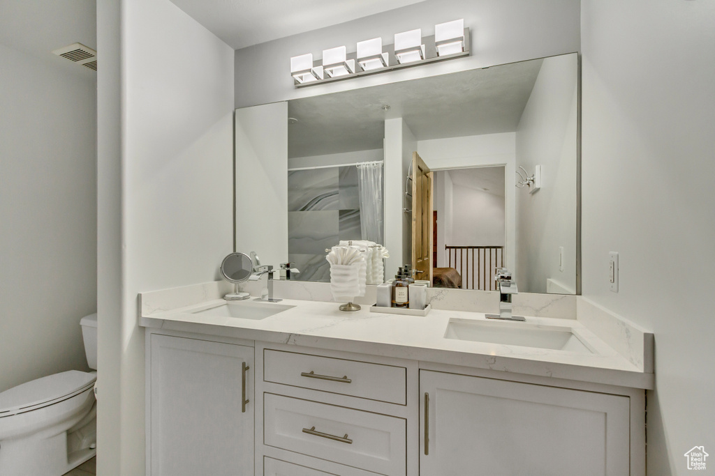 Full bathroom with toilet, double vanity, and a shower with shower curtain