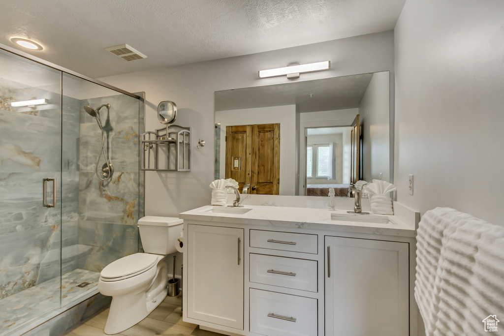 Bathroom with toilet, a marble finish shower, double vanity, wood finished floors, and a textured ceiling