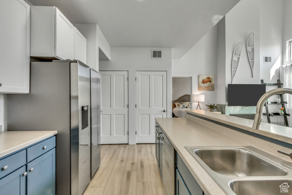 Kitchen with appliances with stainless steel finishes, light wood finished floors, blue cabinetry, light countertops, and white cabinets