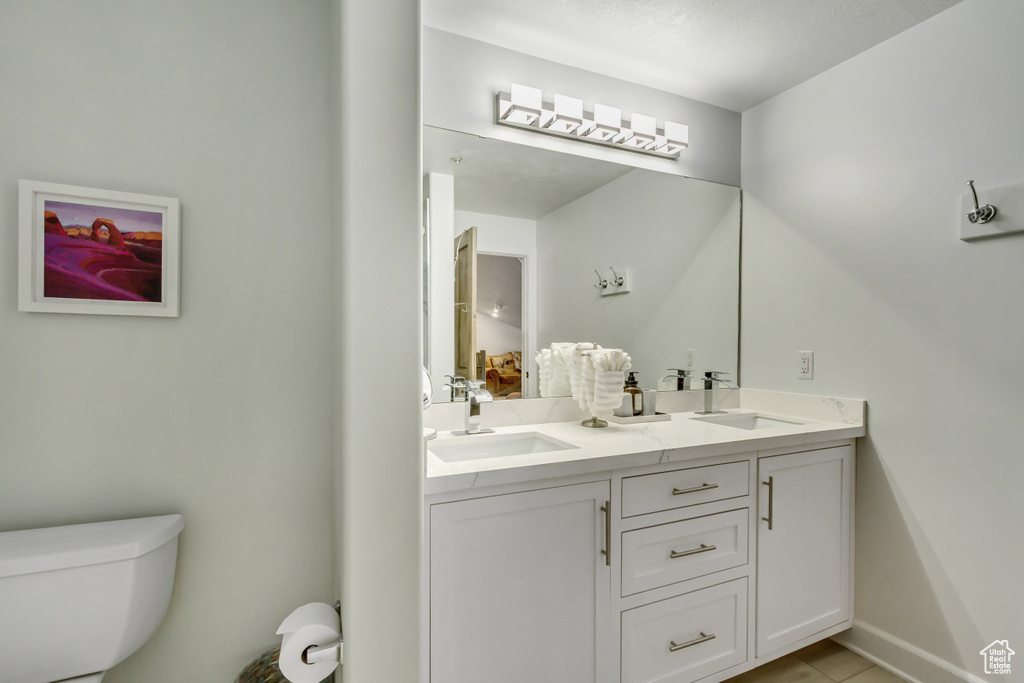 Bathroom with toilet, double vanity, tile patterned floors, and baseboards