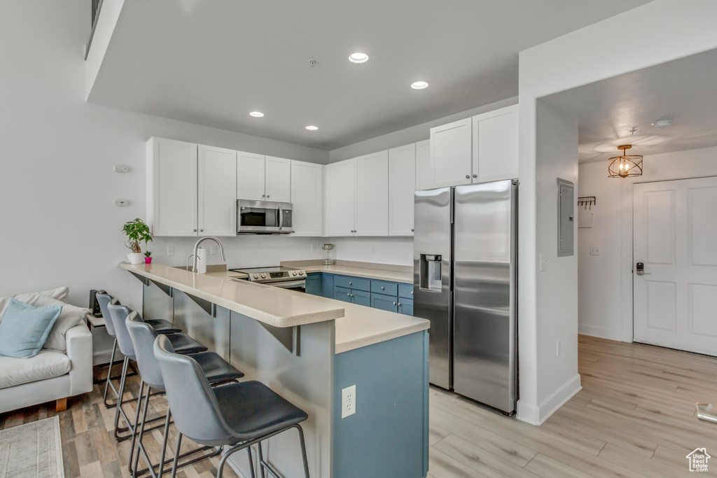 Kitchen featuring appliances with stainless steel finishes, a peninsula, a kitchen bar, blue cabinetry, and recessed lighting