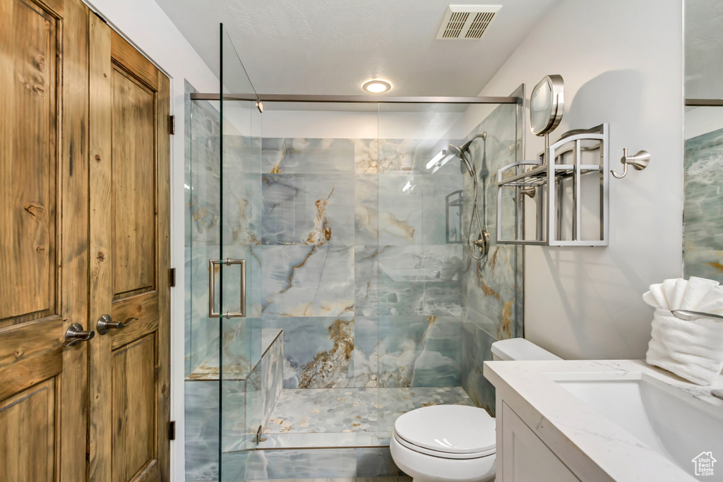 Full bathroom with a marble finish shower, toilet, and vanity