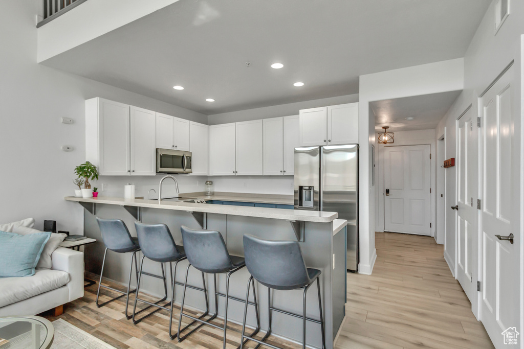 Kitchen with appliances with stainless steel finishes, a peninsula, recessed lighting, a breakfast bar, and light wood-style floors
