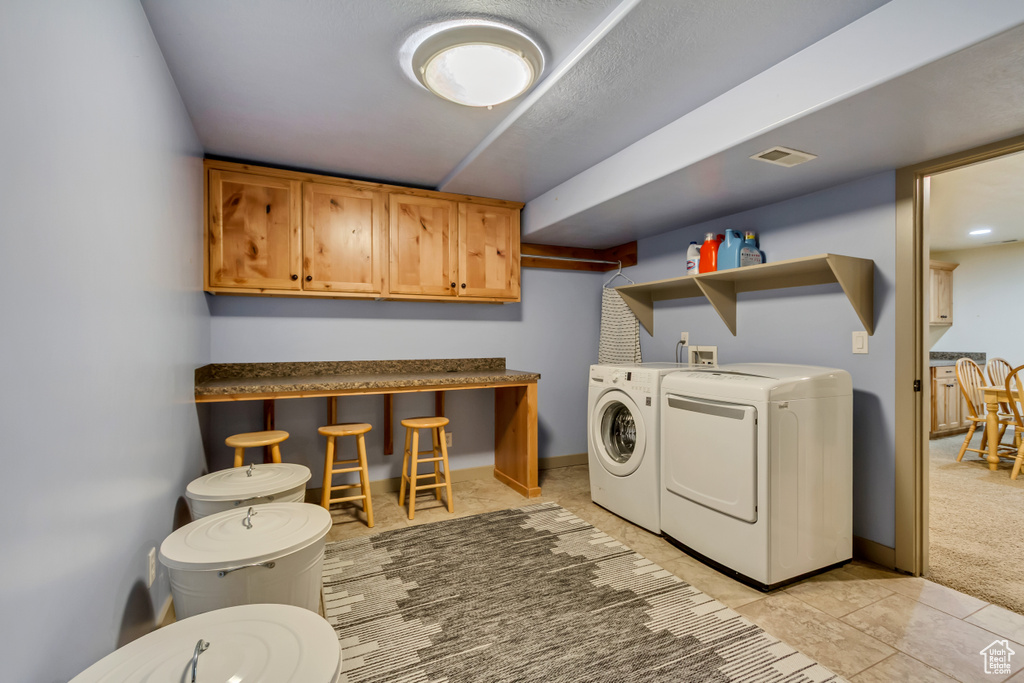 Laundry area featuring washing machine and clothes dryer, cabinet space, light carpet, and light tile patterned floors
