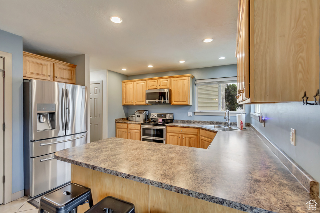 Kitchen with stainless steel appliances, a sink, a peninsula, light brown cabinetry, and recessed lighting