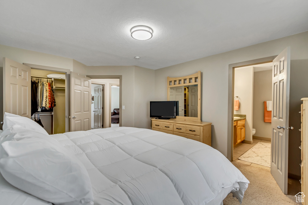 Bedroom featuring ensuite bath, baseboards, a closet, light colored carpet, and a walk in closet
