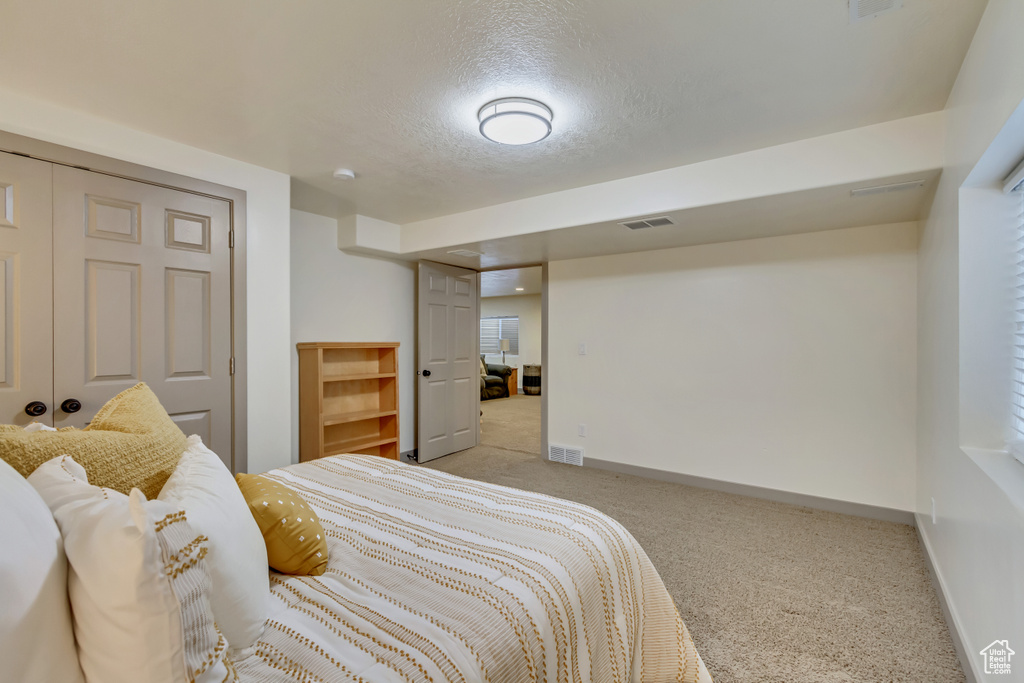 Bedroom with light carpet, baseboards, a textured ceiling, and a closet