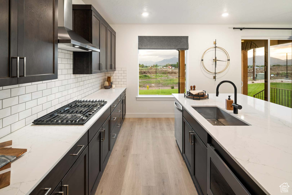 Kitchen featuring a sink, wall chimney exhaust hood, gas cooktop, dishwasher, and baseboards