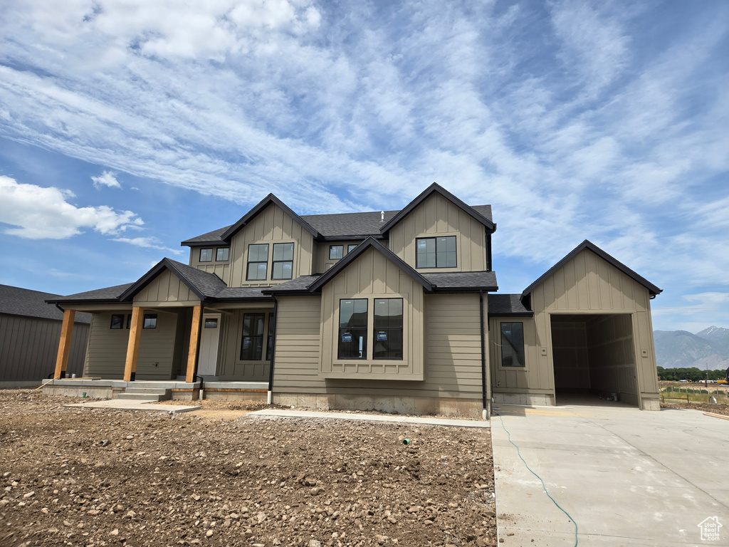 View of front facade featuring board and batten siding, covered porch, a shingled roof, driveway, and a mountain view