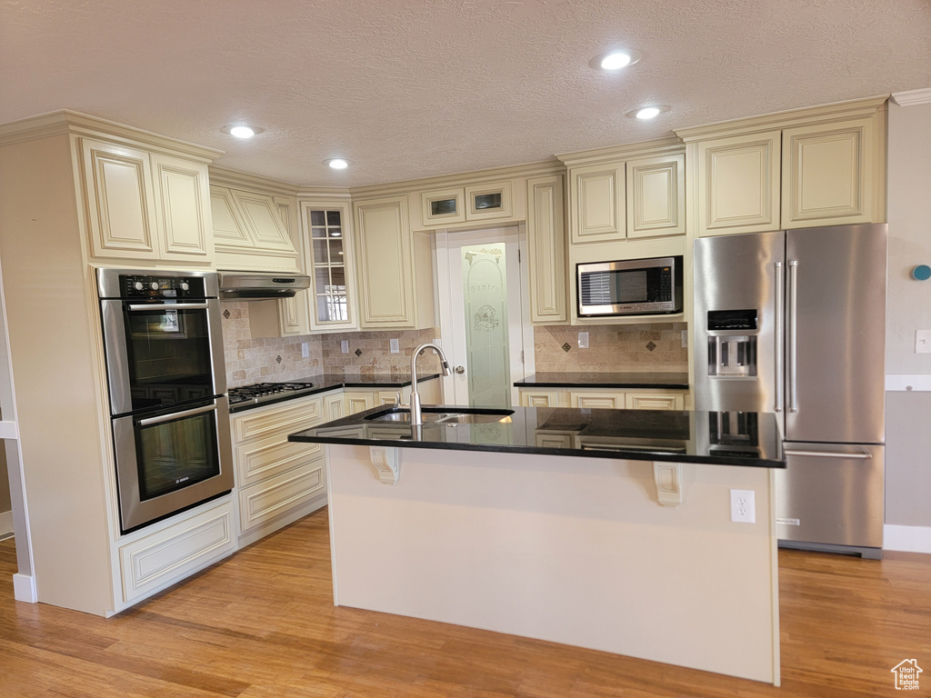Kitchen with cream cabinets, appliances with stainless steel finishes, a sink, dark countertops, and recessed lighting