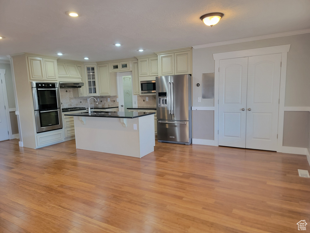 Kitchen featuring appliances with stainless steel finishes, dark countertops, cream cabinetry, light wood-style flooring, and crown molding