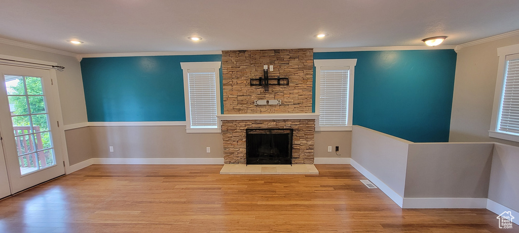 Unfurnished living room with wood finished floors, crown molding, a stone fireplace, baseboards, and recessed lighting