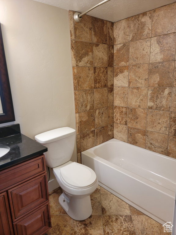 Full bath featuring toilet, vanity, a textured ceiling, bathing tub / shower combination, and stone finish flooring