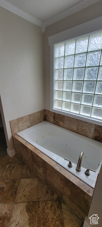 Bathroom with stone tile flooring, a jetted tub, crown molding, and baseboards