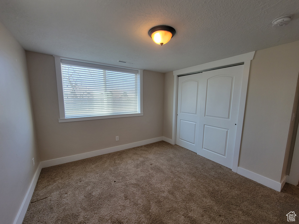 Unfurnished bedroom with carpet floors, a closet, baseboards, and a textured ceiling