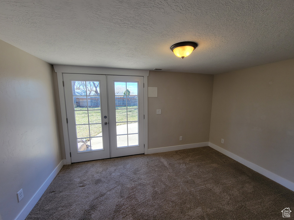 Carpeted spare room featuring french doors, a textured ceiling, and baseboards