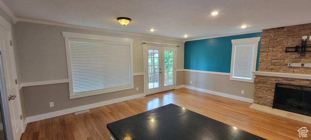 Unfurnished living room featuring french doors, wood finished floors, ornamental molding, baseboards, and a fireplace