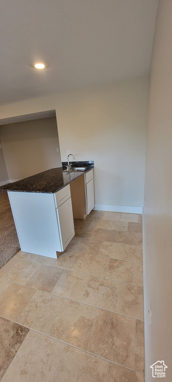 Kitchen featuring dark countertops, stone tile floors, a sink, white cabinets, and recessed lighting