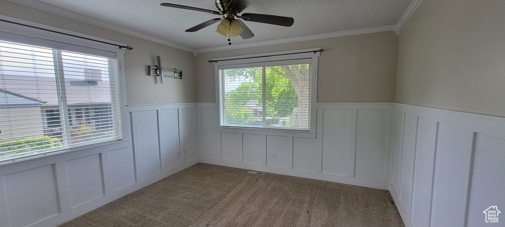 Spare room featuring a decorative wall, a wainscoted wall, ceiling fan, crown molding, and light colored carpet