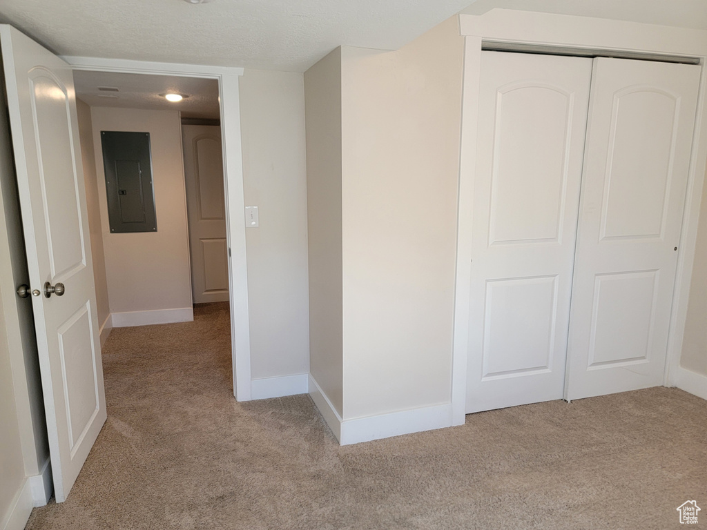 Corridor with light colored carpet, electric panel, and baseboards