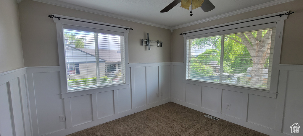 Unfurnished dining area with a decorative wall, wainscoting, carpet floors, and ceiling fan