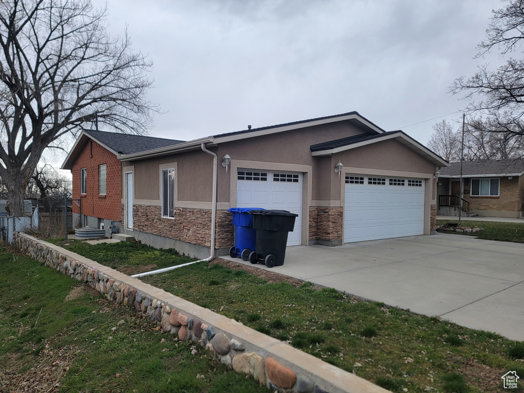 View of front of house featuring a garage, driveway, stone siding, and stucco siding