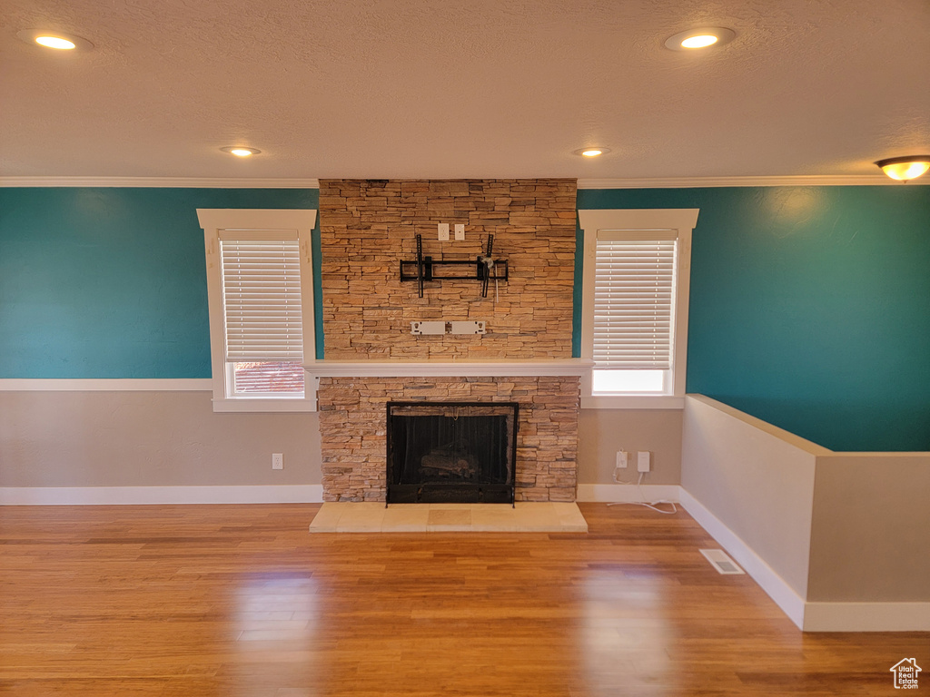 Unfurnished living room featuring a fireplace, ornamental molding, wood finished floors, a textured ceiling, and baseboards